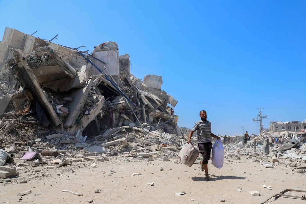 Palestina corre segurando pertences próximo a destroços de prédio derrubado por bombardeio israelense na Cidade de Gaza, na Faixa de Gaza, em 5 de setembro de 2025. — Foto: REUTERS/Ebrahim Hajjaj