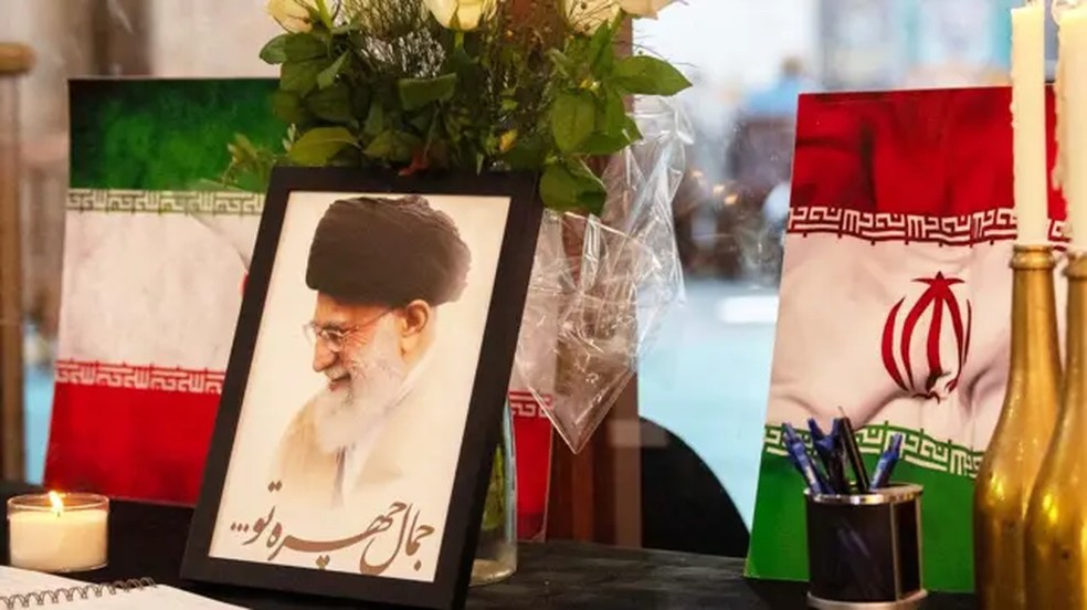 Retrato do líder supremo do Irã, o aiatolá Ali Khamenei, é exibido ao lado de bandeiras iranianas, velas e um livro de condolências em uma mesquita na Cidade do Cabo. — Foto: Getty Images via BBC