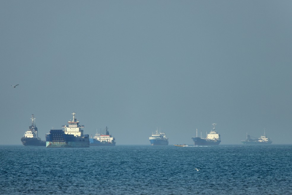 Foto mostra navios ao fundo enquanto uma pequena lancha passa em primeiro plano no Estreito de Ormuz, ao largo de Bandar Abbas, no Irã, na segunda-feira, 4 de maio de 2026. — Foto: Amirhosein Khorgooi/ISNA via AP
