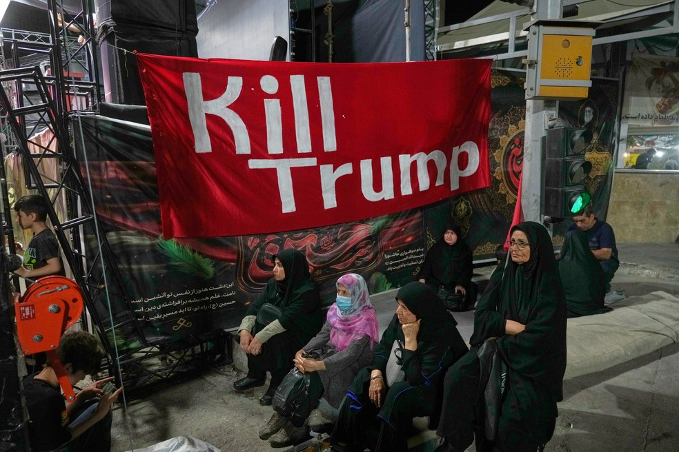 Mulheres sentam-se ao lado de uma faixa com os dizeres "Matem Trump" em inglês, durante um comício pró-governo na sexta-feira, 17 de julho de 2026, em Teerã, Irã — Foto: AP/Vahid Salemi